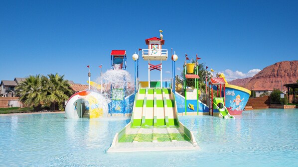 A water park with a central water slide, multiple water features, and a mountain backdrop.
