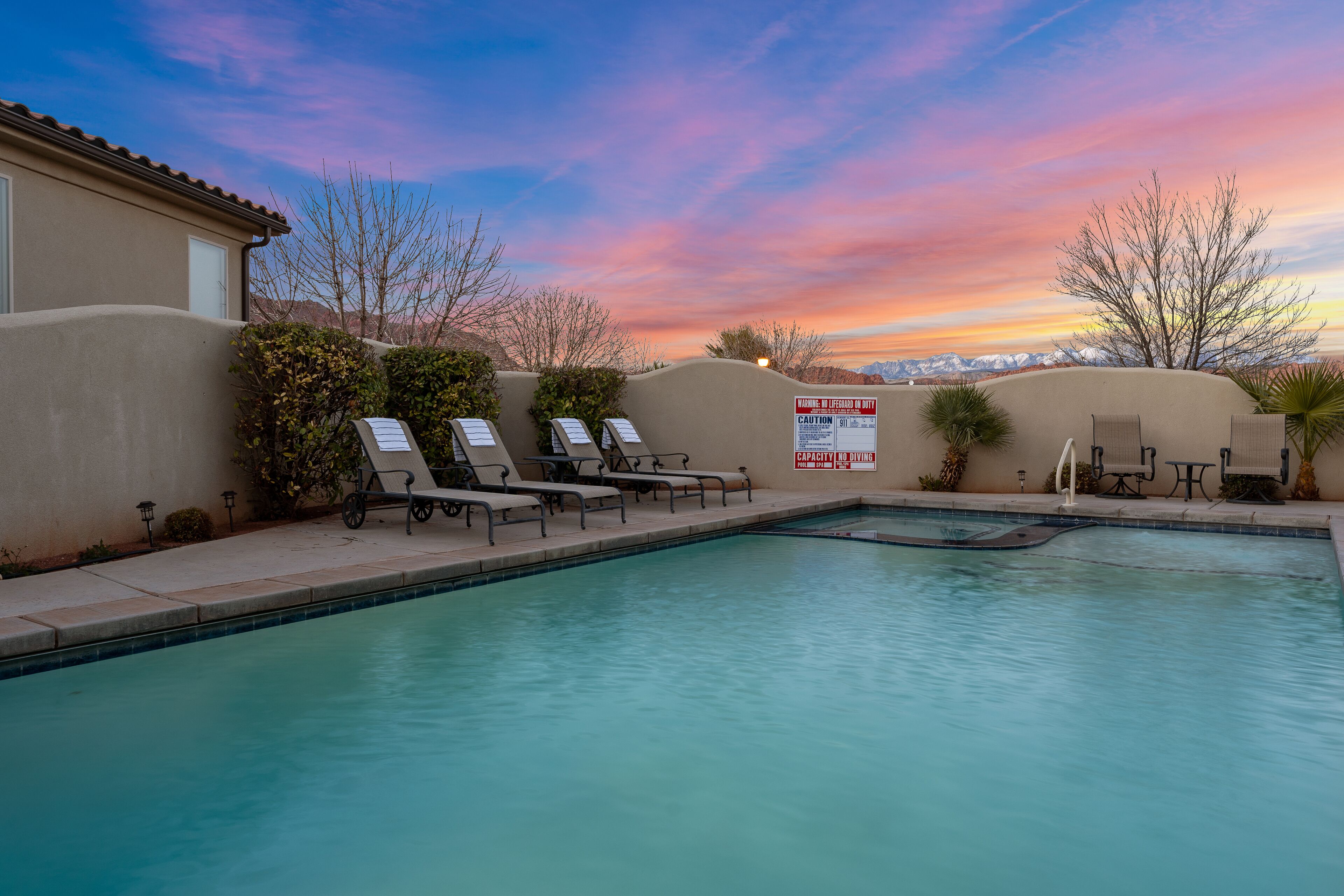 A swimming pool with lounge chairs and a view of mountains during sunset.
