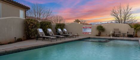 A swimming pool with lounge chairs and a view of mountains during sunset.