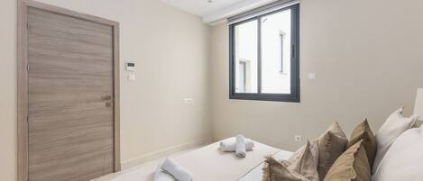 Habitación de hotel con un ventanal grande, una cama con toallas dobladas, una puerta de madera y un termostato en la pared.