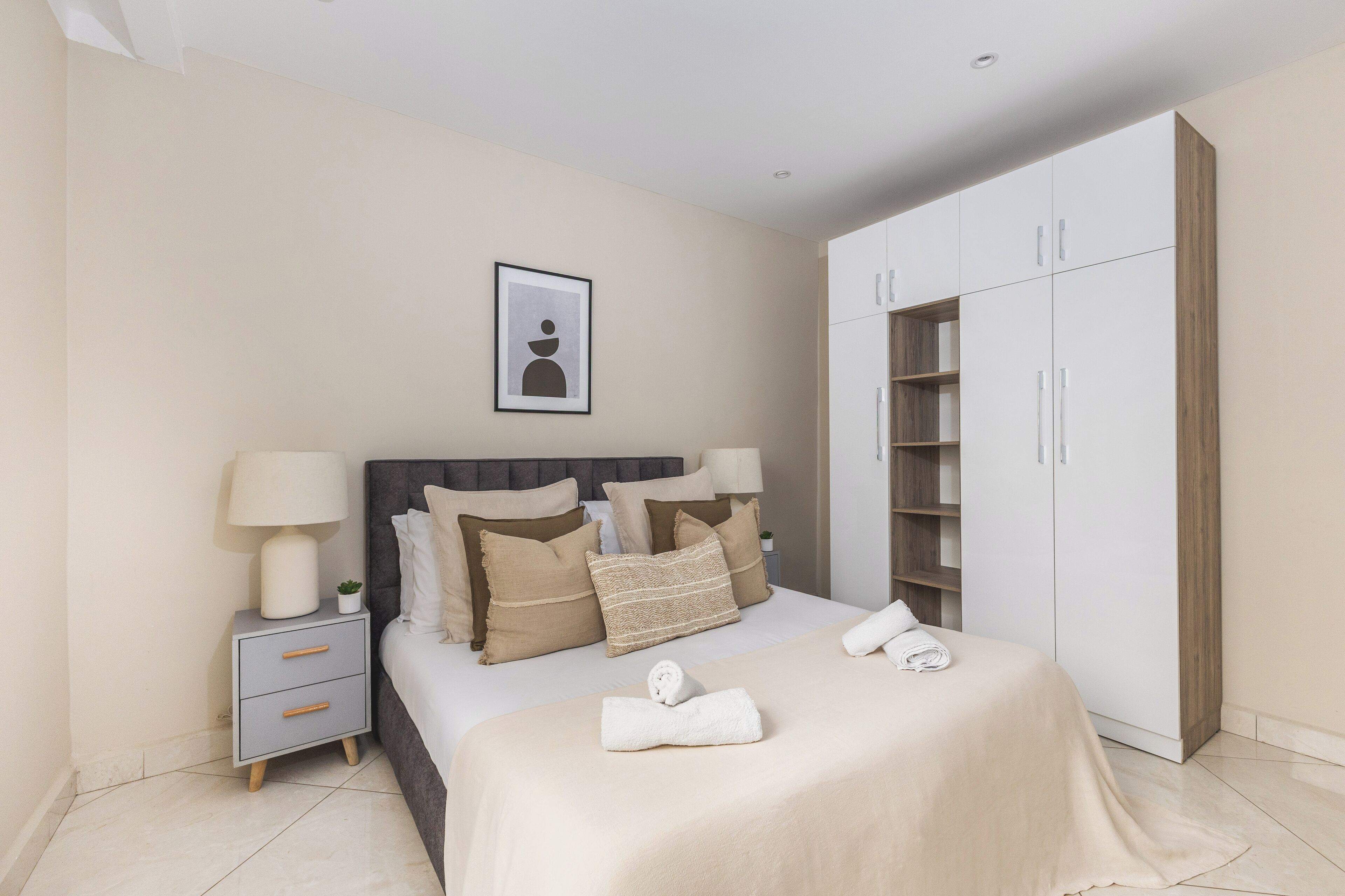 A modern bedroom with a bed, nightstands, a wardrobe, and a framed picture on the wall.