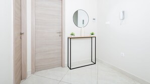 Un pasillo con una puerta de madera, un espejo redondo sobre un atril de metal negro y una pequeña planta en maceta.