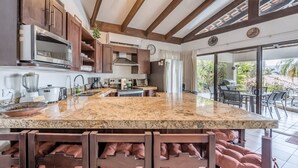 A modern kitchen with a granite countertop, wooden cabinets, and a large island with bar stools. - Beautiful 3 bedroom and 2 bathrooms villa close to beach. (Playa Hermosa)