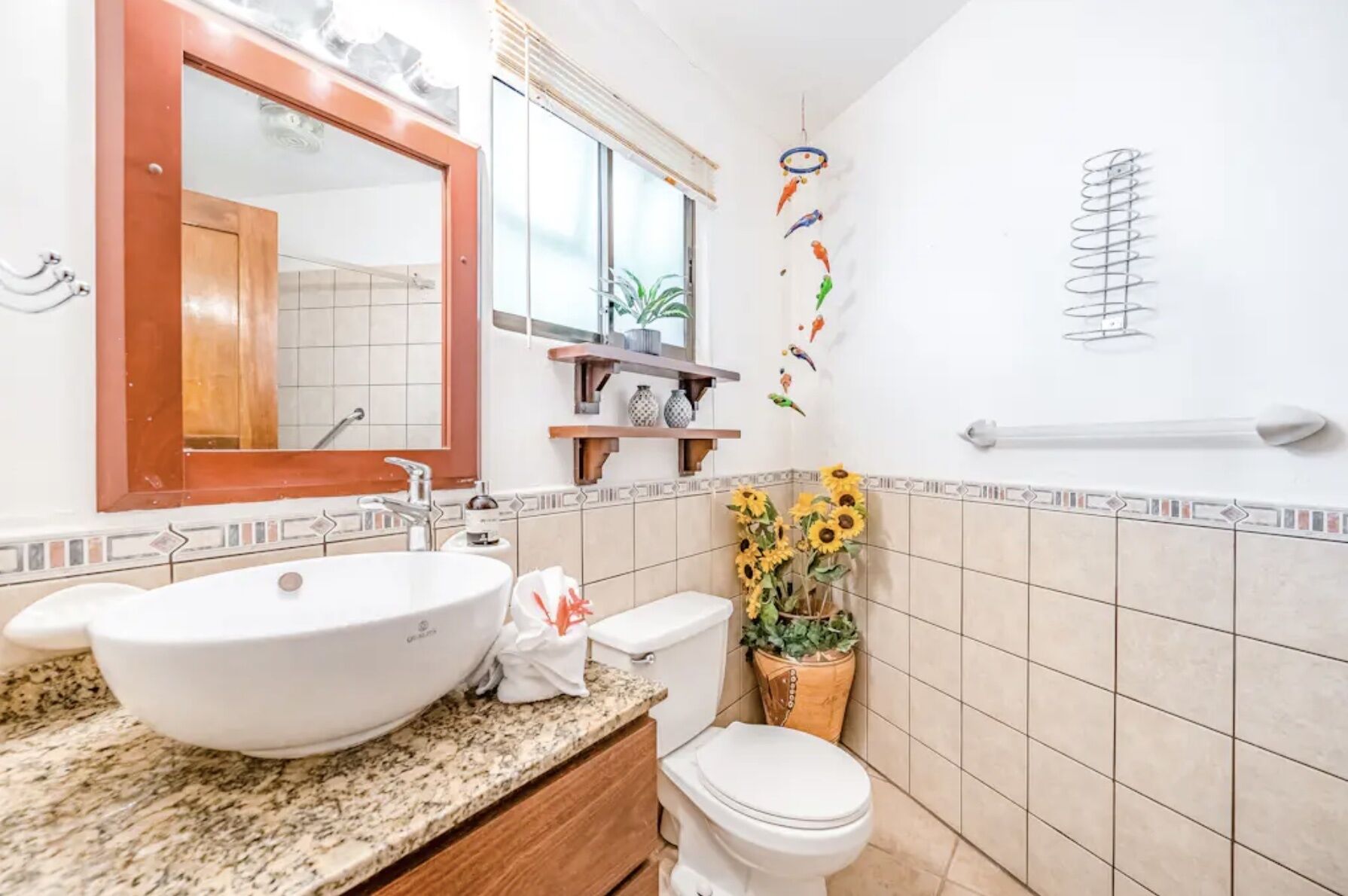 Un bagno con un lavandino bianco grande, un WC, uno specchio e uno scaffale con oggetti decorativi.