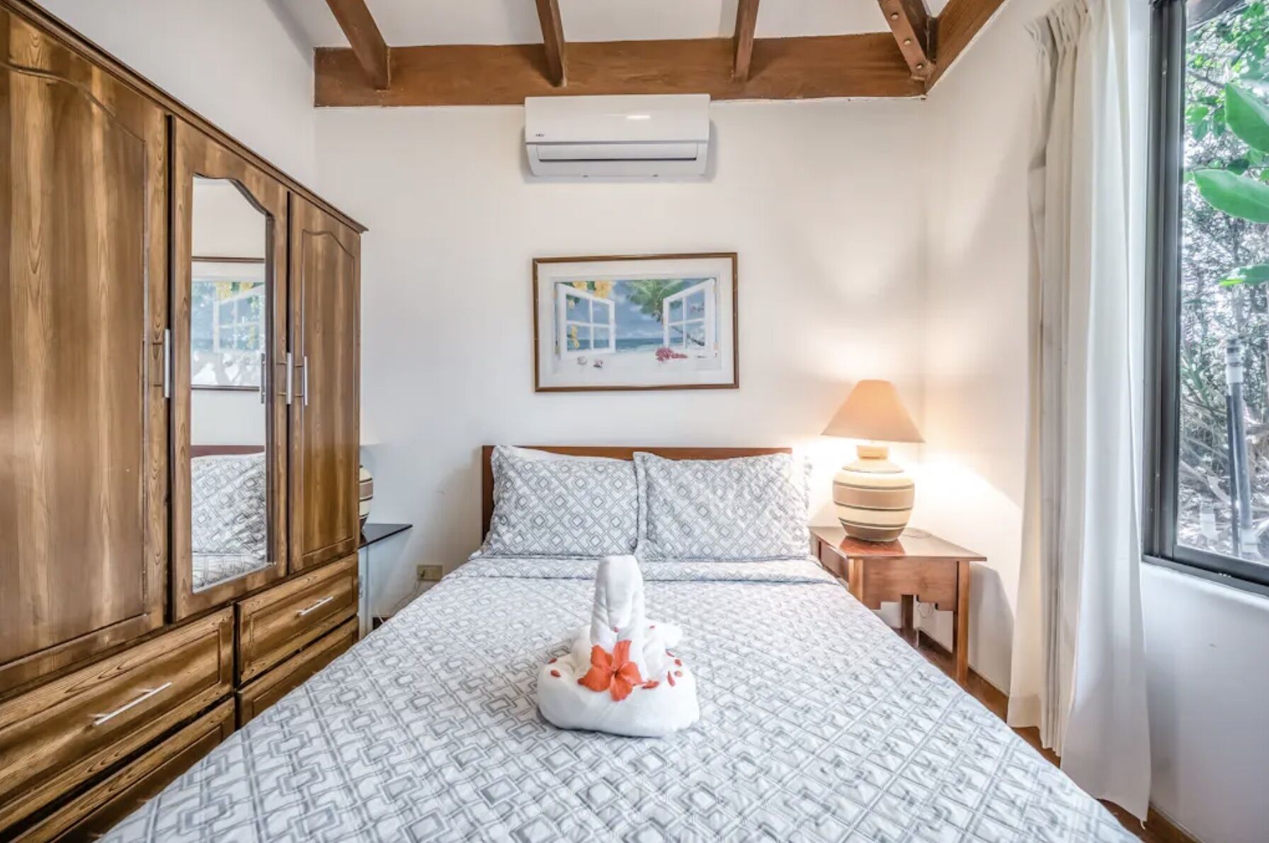 A bedroom with a bed, a wooden wardrobe, a framed picture on the wall, and a window with curtains.