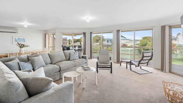 A spacious living room with a grey sofa, a round coffee table, and a dining area with white chairs. - Strandhytta 10 Cant Rd Goolwa South (Goolwa South)
