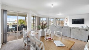 A modern living room with a dining area, large windows, and a flat-screen TV. - Strandhytta 10 Cant Rd Goolwa South (Goolwa South)