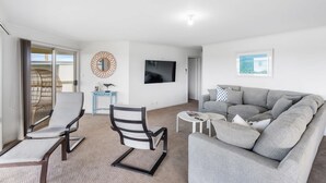 A living room with a grey sofa, a white armchair, a small table, a TV, and a decorative mirror. - Strandhytta 10 Cant Rd Goolwa South (Goolwa South)