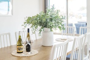 Une table à manger avec deux bouteilles de vin, un vase rempli de feuillage vert et des chaises blanches.