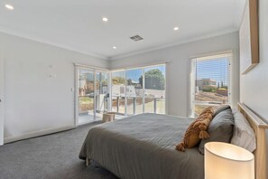 Une chambre à coucher avec un lit, une lampe et de grandes fenêtres équipées de stores.