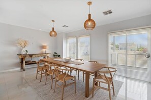 Un espace repas avec une table en bois, des chaises, des luminaires suspendus et une vue dégagée grâce à de grandes fenêtres.