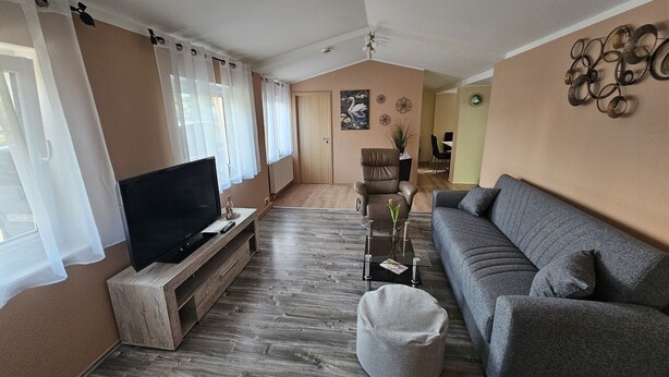 Una sala de estar con un televisor sobre un soporte de madera, un sofá gris, una mesa de centro y una mesita con un jarrón.
