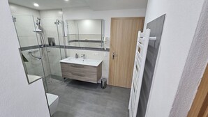 Un baño moderno con ducha envuelta en vidrio, tocador con lavamanos y puerta de madera.