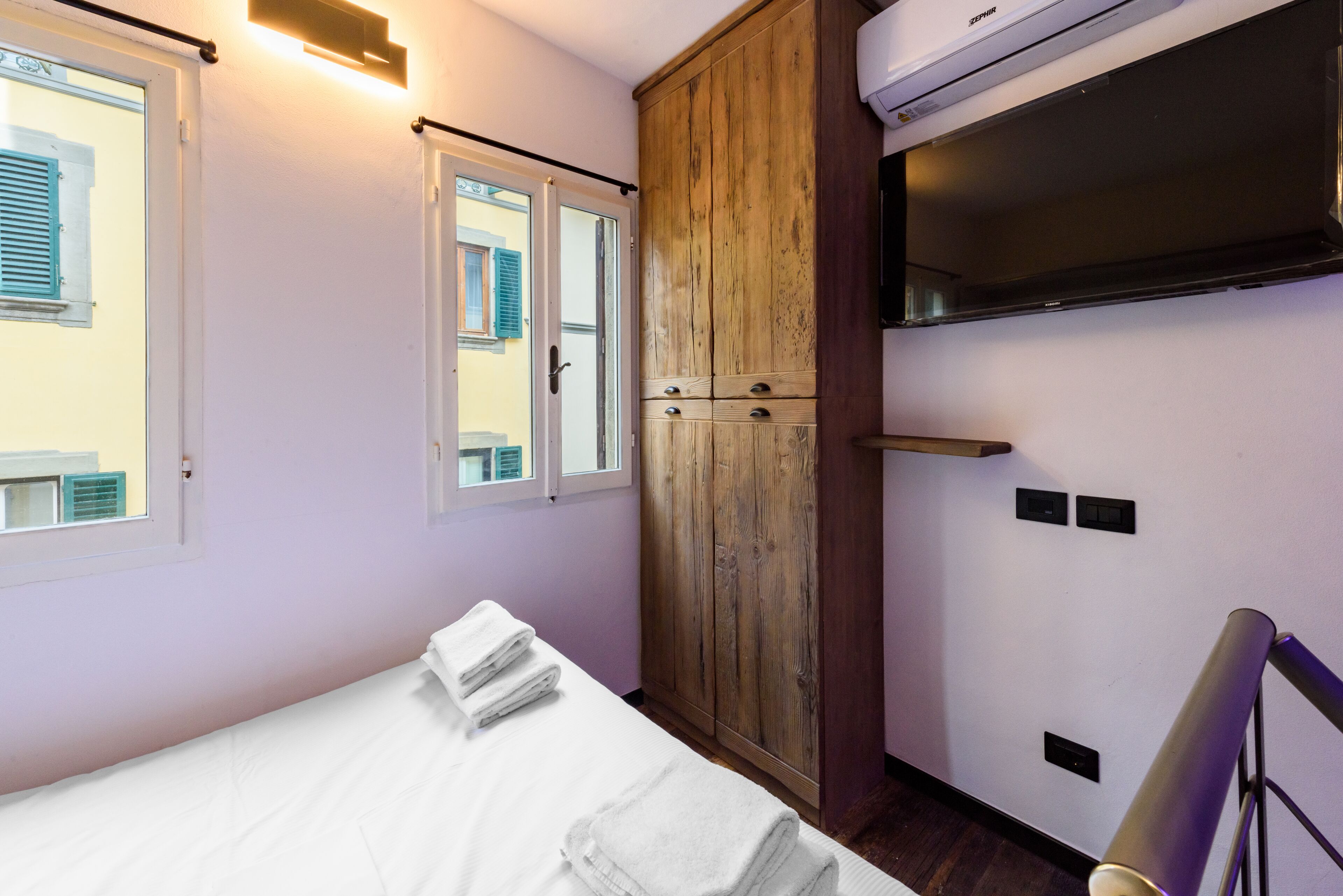 A bedroom with a bed, a wooden wardrobe, and a window with shutters.