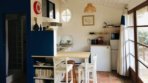 Une cuisine compacte comprenant un coin repas, un petit réfrigérateur, un évier et une fenêtre avec des rideaux.