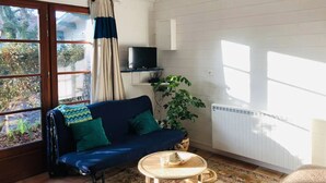 Une pièce avec un canapé bleu, une petite table ronde, une plante en pot et un téléviseur accroché à un mur blanc.