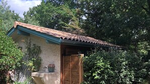 Un petit bâtiment en pierre, avec un toit en tuiles et une porte en bois, entouré d’une végétation luxuriante.