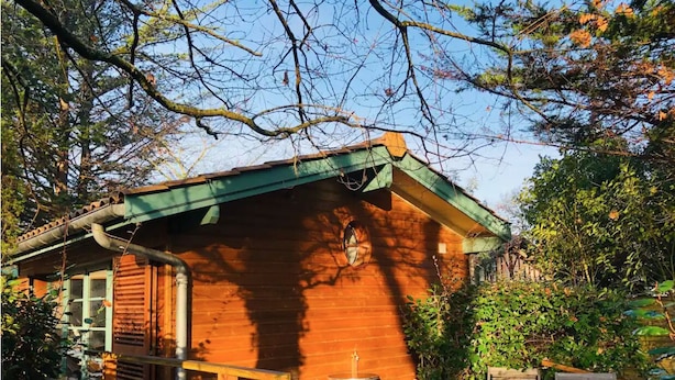 Une cabane en bois avec un toit vert, une petite véranda et une table avec des chaises.