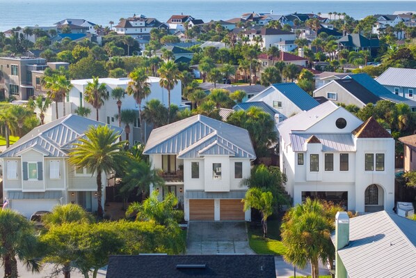 A residential area with houses featuring modern architecture, surrounded by lush greenery and palm trees.
