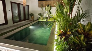 A swimming pool surrounded by lush greenery and a modern building with large windows and a wooden fence. - Villa Flora - Seseh Area (Munggu)