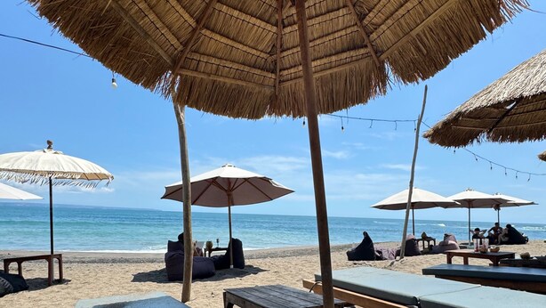 A beach with thatched umbrellas, lounge chairs, and wooden tables. - Villa Flora - Seseh Area (Munggu)