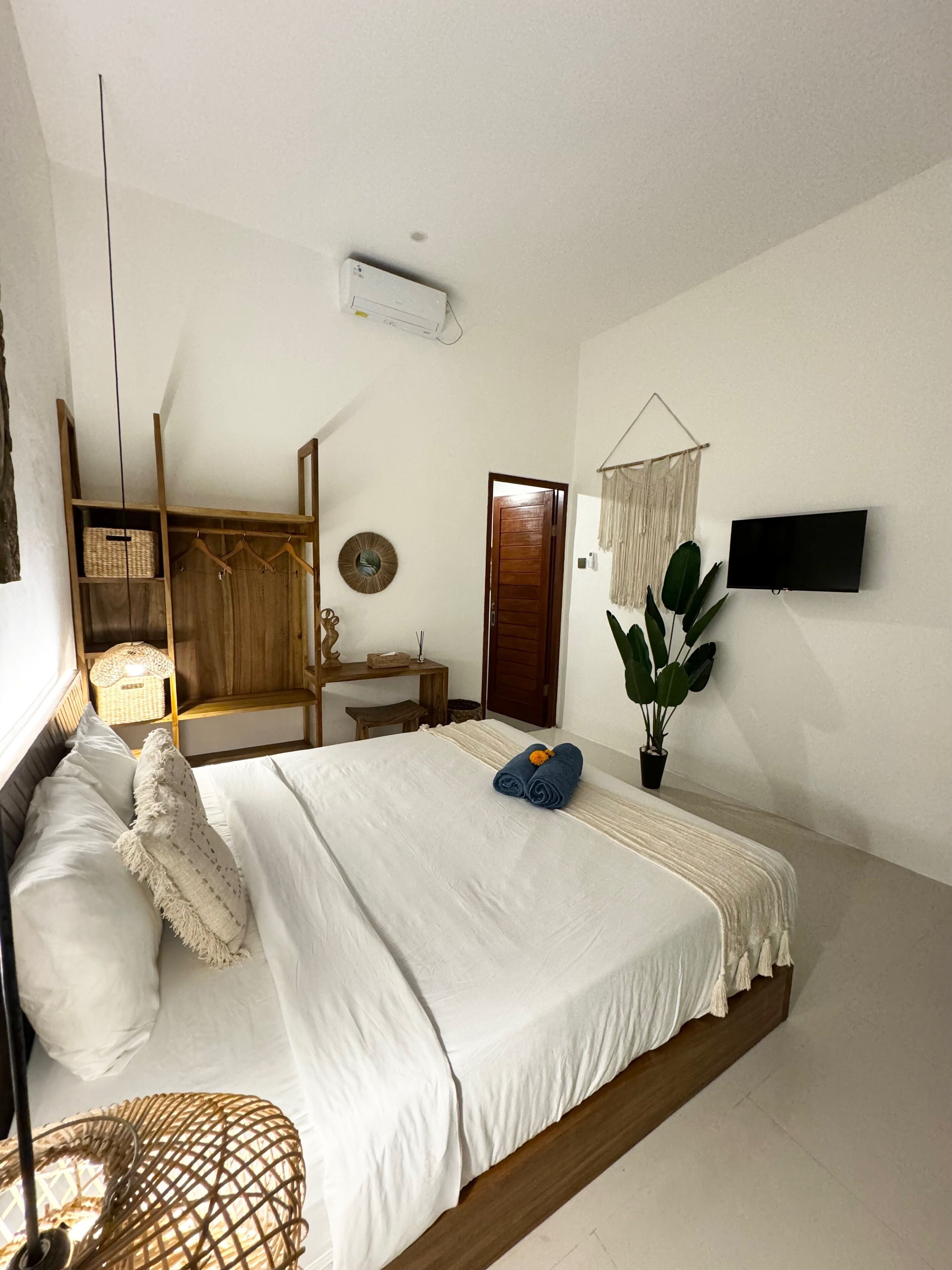 Ein Schlafzimmer mit einem Bett, einem Holzschrank, einem Schreibtisch, einer hängenden Pflanze und einem an der Wand befestigten Fernseher.