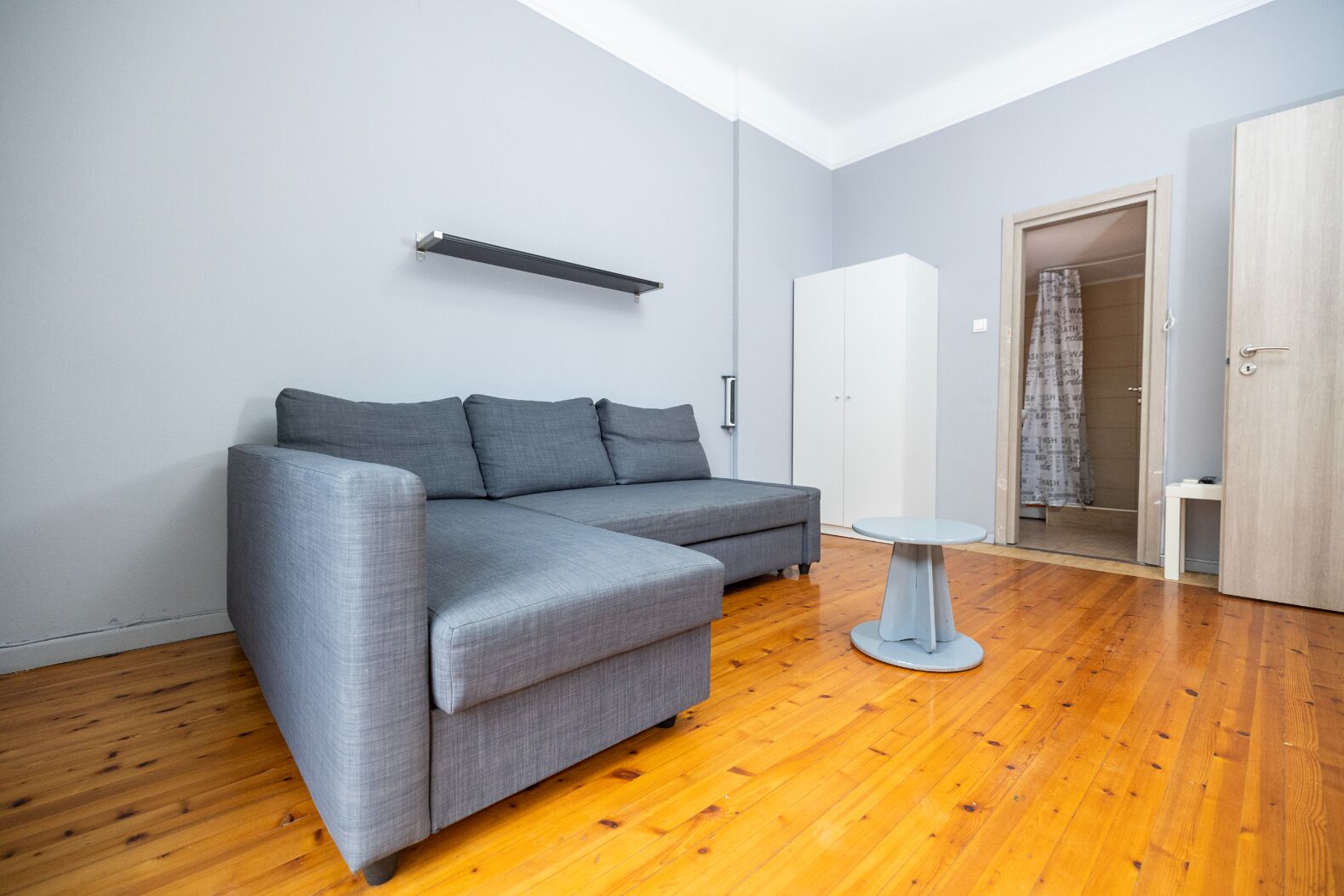 Ein modernes Wohnzimmer mit einem grauen Ecksofa, einem kleinen runden Tisch und einem Kleiderschrank.