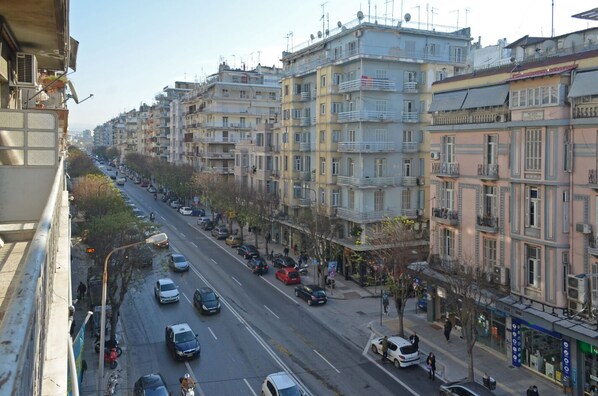 A multi-story building with balconies, a street with parked cars, and pedestrians.