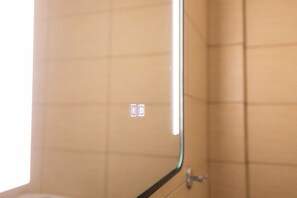 A bathroom with a tiled wall and a mirror reflecting a light fixture.