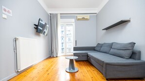 A modern living room with a grey sectional sofa, a small round table, and a white radiator. - Egnatia Central Spacious 3 Bd Apt (Thessaloniki)
