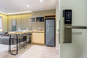 A modern kitchen with a built-in microwave, a grey refrigerator, and a dining area with a table and chairs. - House Of Charlie Apartments Pinheiros - Soft Opening (São Paulo)