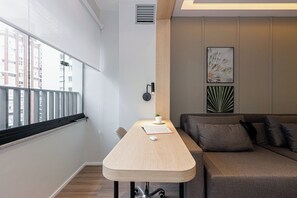 A modern room with a wooden desk, a sofa, and a window with a view of buildings. - House Of Charlie Apartments Pinheiros - Soft Opening (São Paulo)