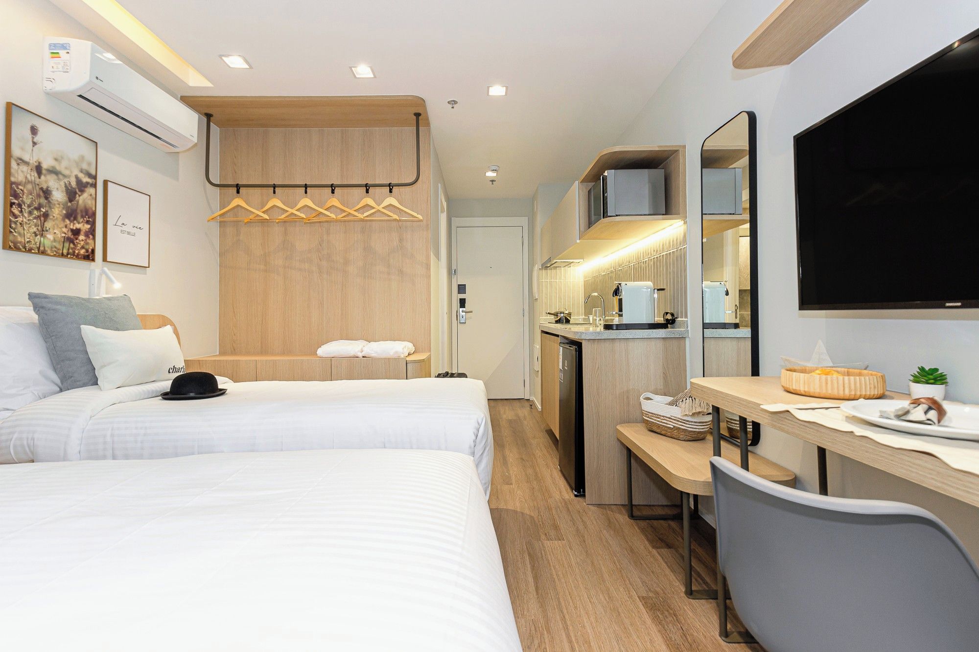 A hotel room with a bed, a desk, a kitchenette, and a TV.