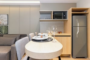 A modern kitchen with a microwave, a refrigerator, and a dining area with a table set for two. - House Of Charlie Apartments Pinheiros - Soft Opening (São Paulo)