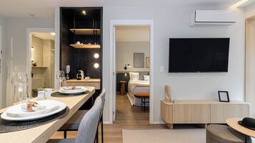 A modern hotel room with a dining area, a bed, a TV, and a bathroom visible through an open door.