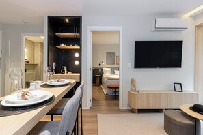 A modern hotel room with a dining area, a bed, a TV, and a bathroom visible through an open door. - House Of Charlie Apartments Pinheiros - Soft Opening (São Paulo)