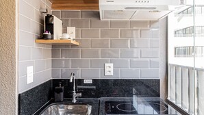 A compact kitchen with a black countertop, white cabinets, a microwave, and a sink. - House of Charlie Pinheiros (São Paulo)