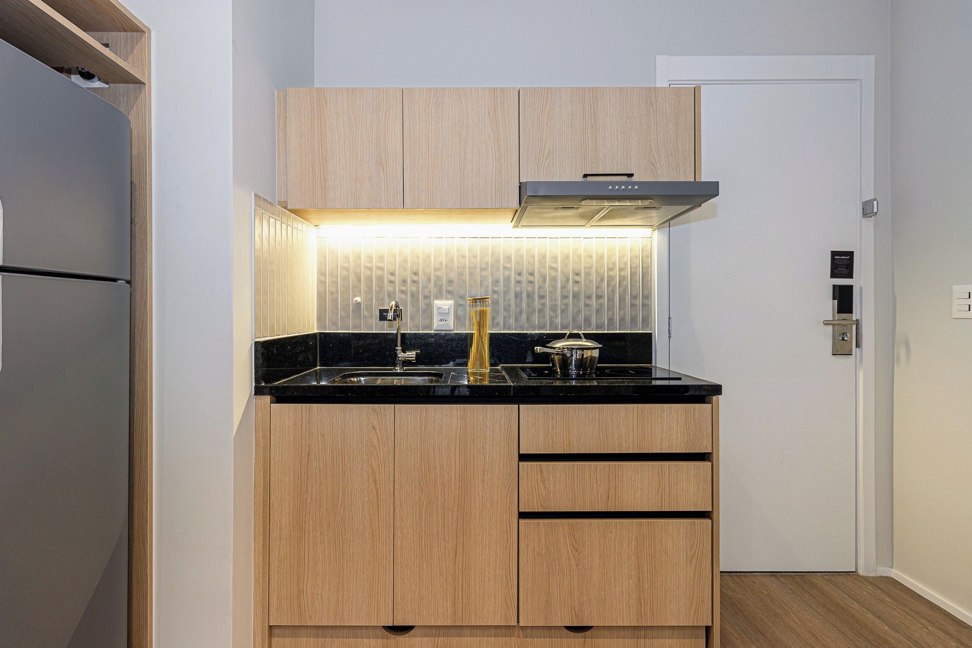 A compact kitchen with wooden cabinets, a black countertop, and a stainless steel range hood.