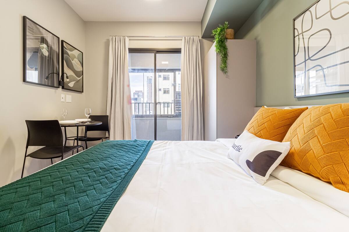 A hotel room with a bed, a desk, and a view of the city through the window.