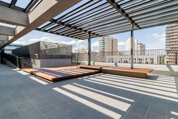 A rooftop terrace with a pergola, seating areas, and a view of surrounding buildings.