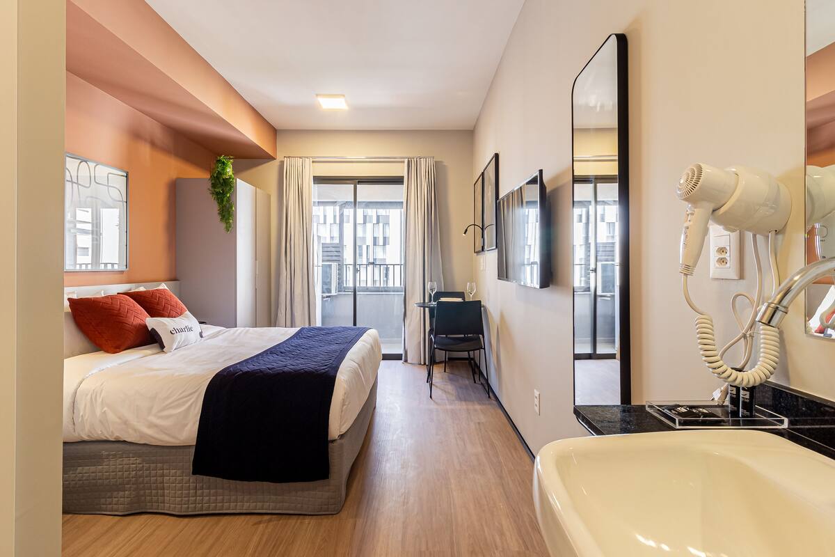 A hotel room with a bed, a desk, a chair, a mirror, and a hairdryer.