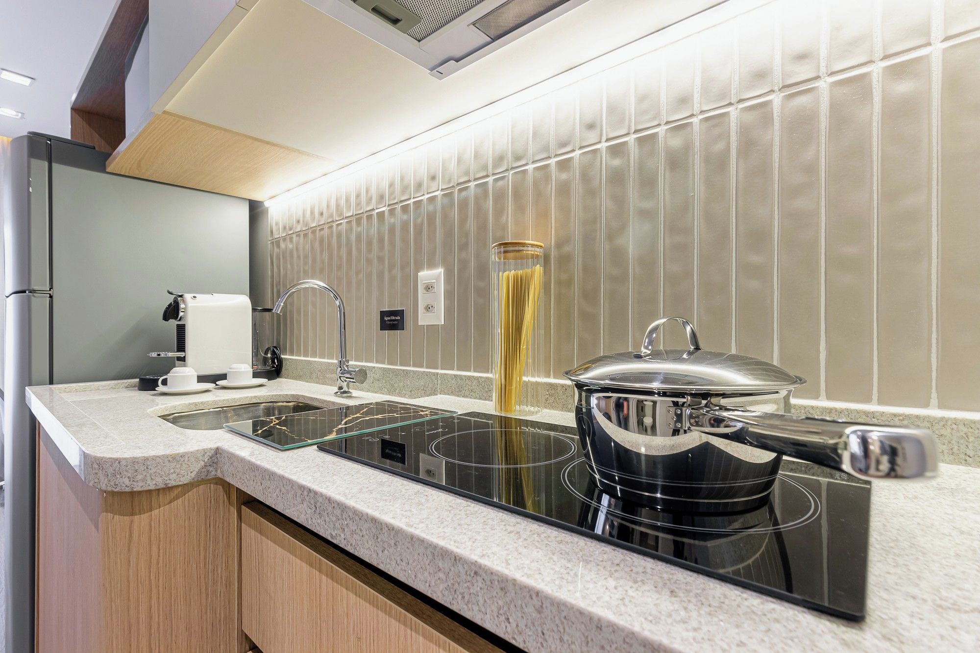 A modern kitchen with a built-in stove, a coffee machine, and a tall glass container of pasta.