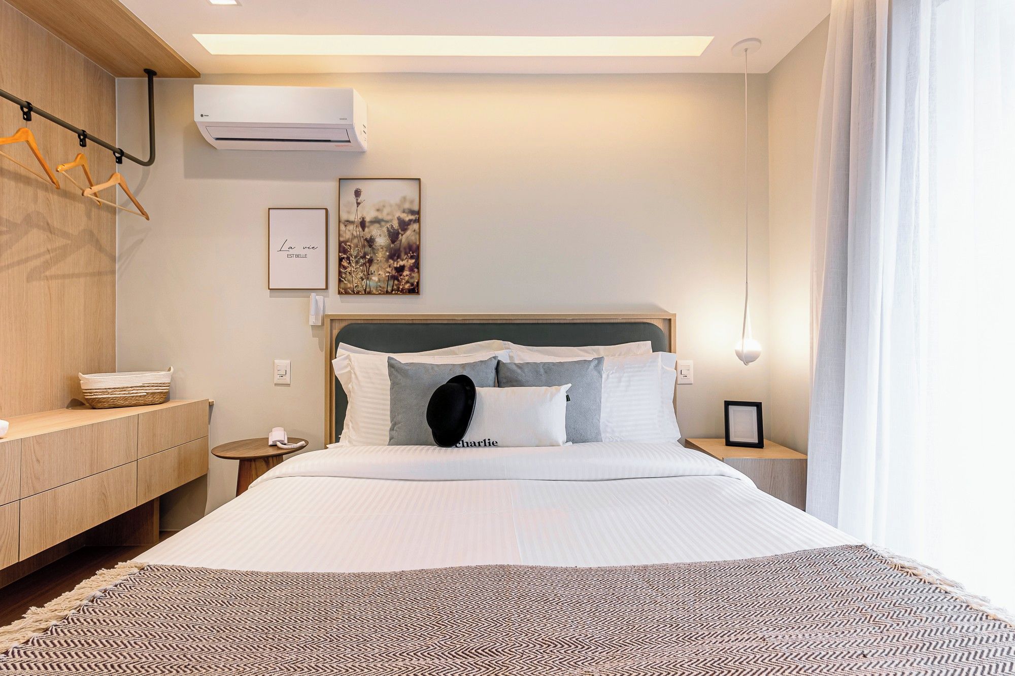 A hotel room with a bed, bedside tables, a wall-mounted air conditioner, and a hanging coat rack.