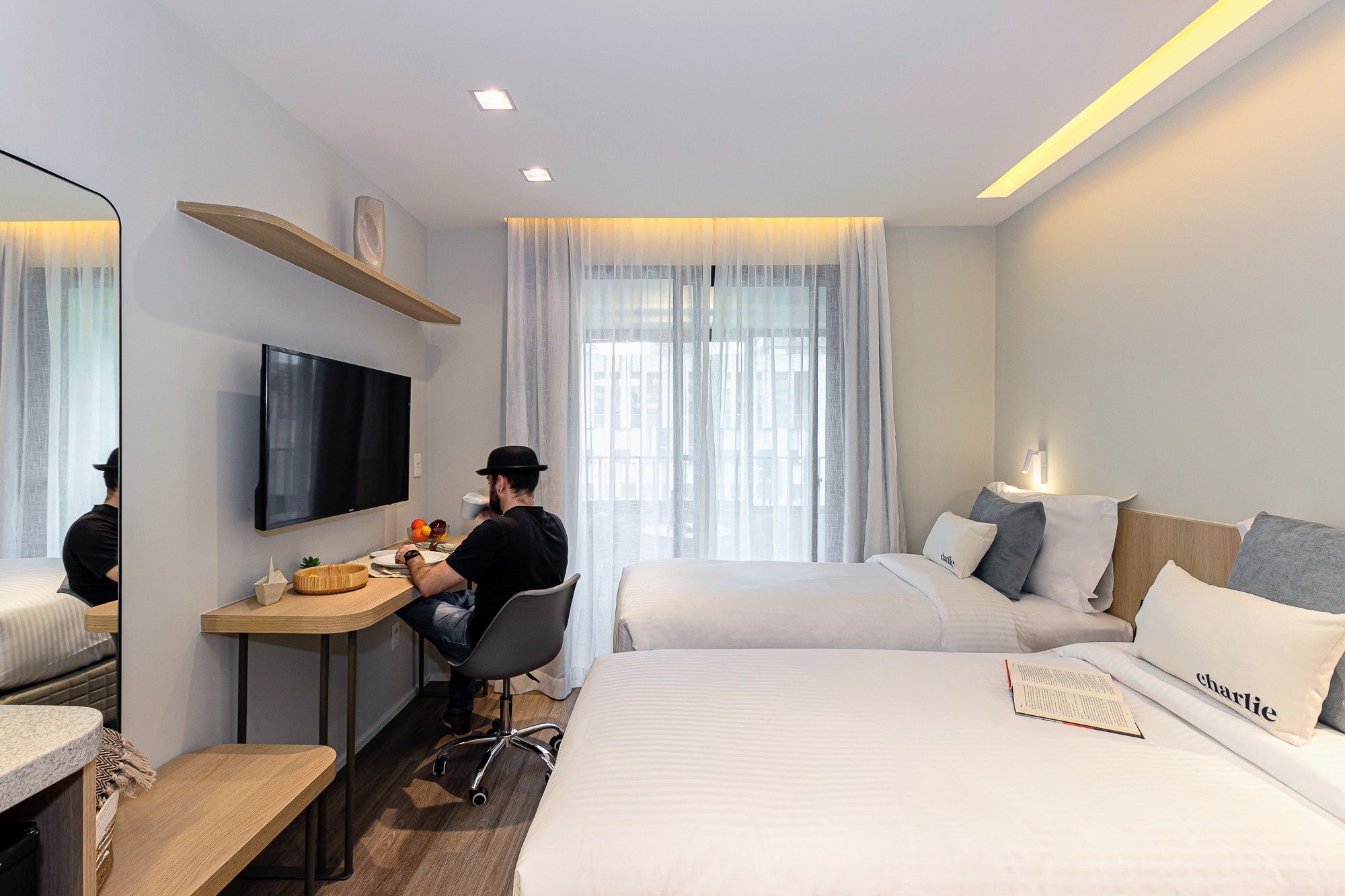 A hotel room with a desk, two beds, a TV, and a window with curtains.