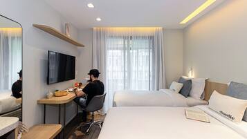 A hotel room with a desk, two beds, a TV, and a window with curtains.