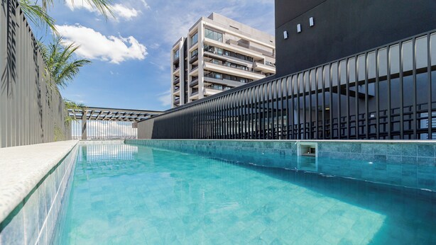 A swimming pool with a clear blue water, surrounded by a modern building with balconies and a metal fence. - House of Charlie Pinheiros (São Paulo)