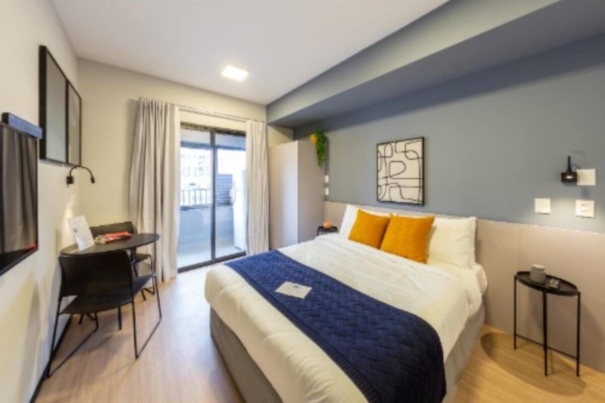 A modern hotel room with a large bed, a desk, and a view of the outside.