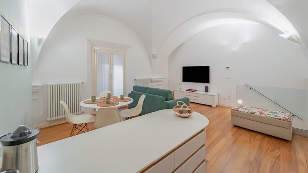 Ein modernes Wohnzimmer mit einem weißen Sofa, einem Esstisch mit Stühlen und einem Fernseher auf einem Standfuß.