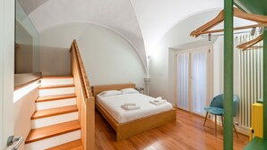 Ein Schlafzimmer mit einer Holztreppe, einem Bett mit weißen Leinen, einem blauen Sessel und einer grünen Wand.