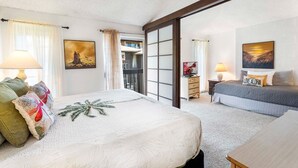 A hotel room with a large bed, a smaller bed, a desk, and a balcony with a view.